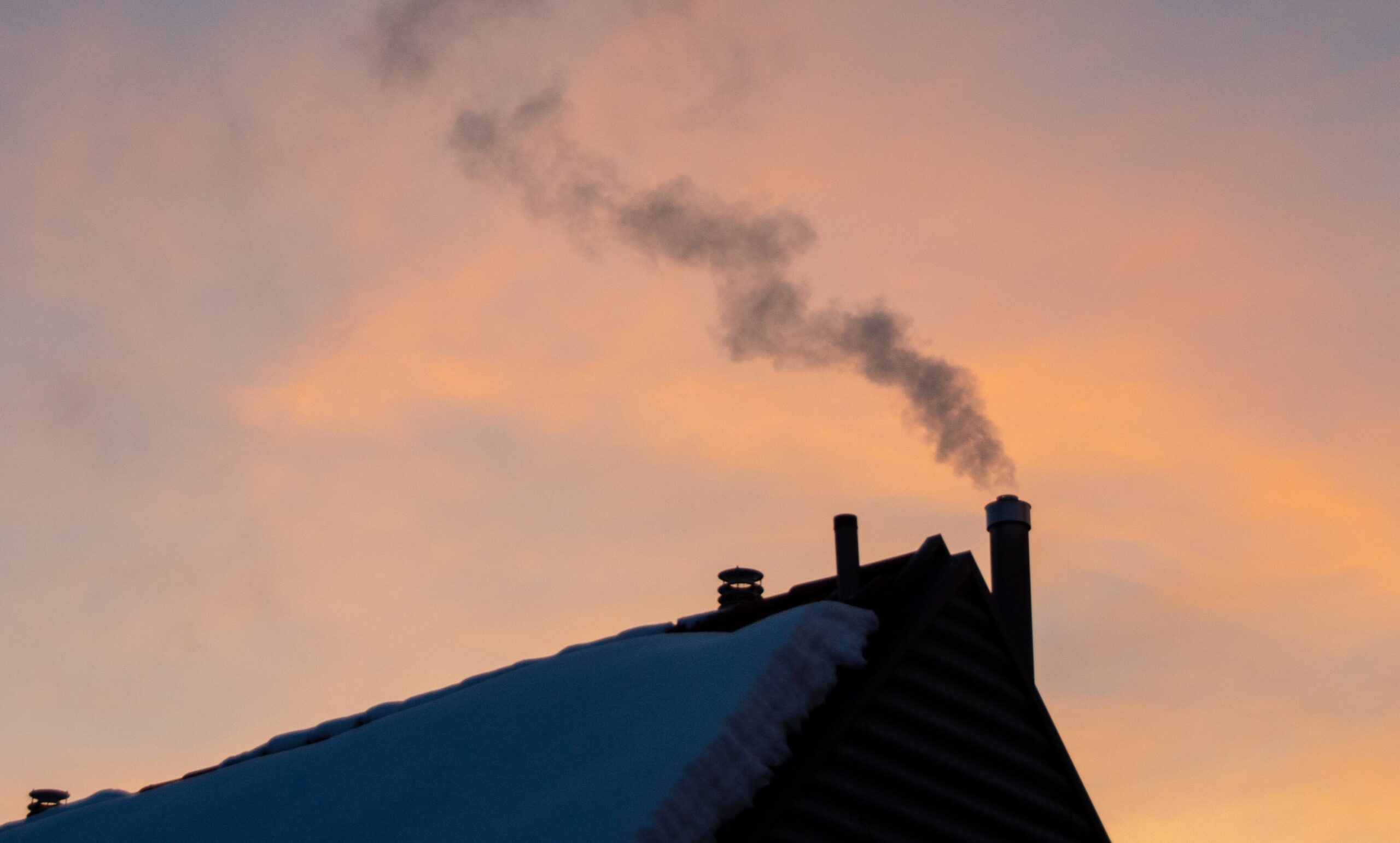 a roof of a house with snow and smoke coming from the chimney